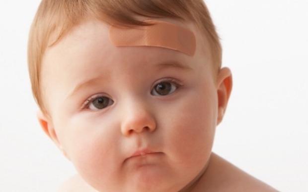 Shows an infant with a bandaid on his forehead