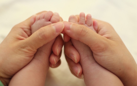 Shows an adult set of hands holding the feet of an infant