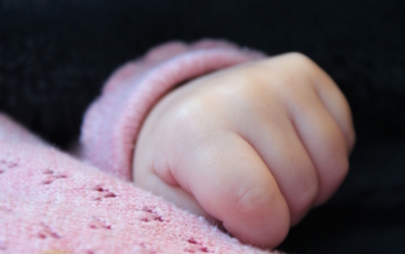 Shows a sleeping baby's hand on top of a pink baby blanket