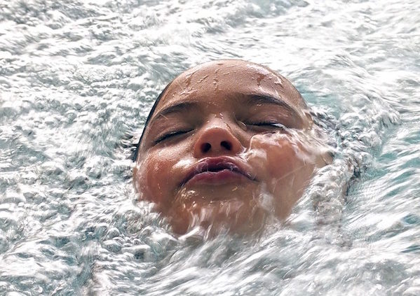 Shows a young child submerged in water with only his face showing