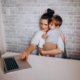 Shows a woman at a desk holding an infant while she is trying to type on a laptop