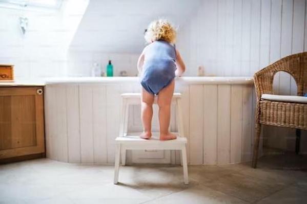 Shows a toddler on a small step stool climbing into a bathtub