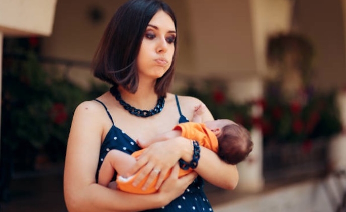 Shows a young mother in a blue dress looking tired and overwhelmed while holding a small baby